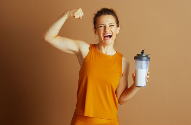 Photo of a smiling, fit woman holding a protein shake